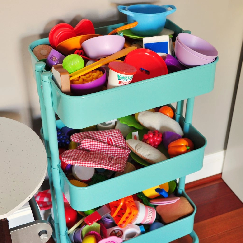 A teal blue three-tiered rolling storage cart from IKEA is great for toy storage in a cluttered playroom.