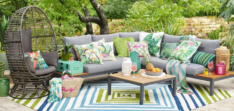 affordable outdoor furniture from t Home - an outdoor sofa accessorized with colorful throw pillows, a stylish outdoor rug, table, and wicker egg-shell chair.