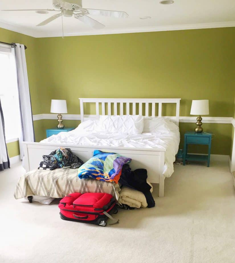 A plain master bedroom with a queen size bed, packed suitcases from moving in, and bright green walls.