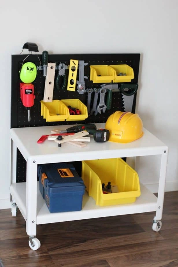 This white IKEA coffee table on wheels is upgraded into a kids play workstation with construction tools hanging on a black pegboard, a hardhat and toy tool boxes.