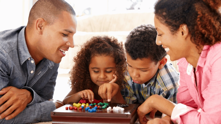 A mom, dad, son, and daughter gather together, playing a board game at home.