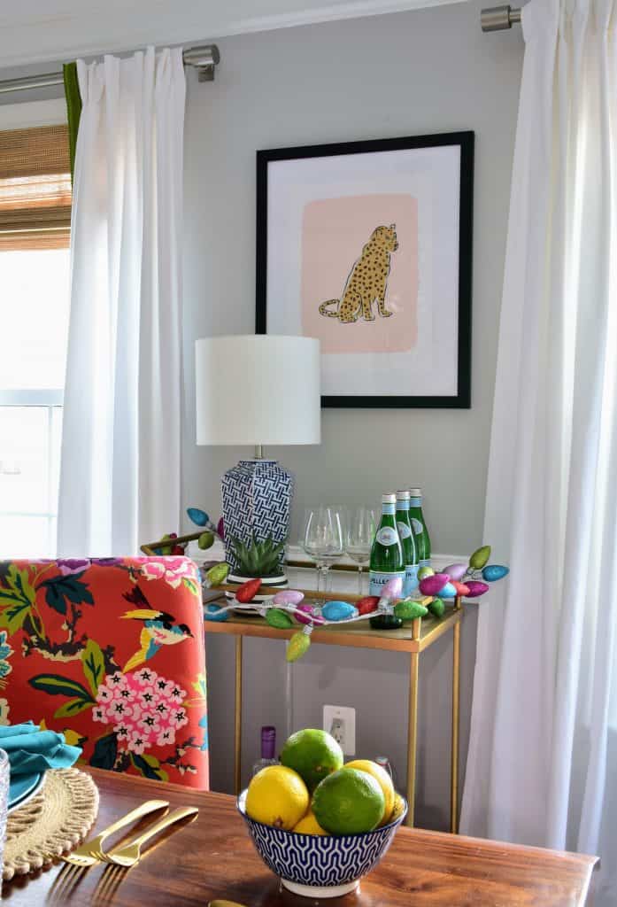 Christmas light garland lines the gold bar cart in our dining room, which sits under a framed art print of a cheetah.
