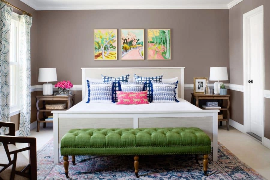 A colorful updated master bedroom with blue and white throw pillows, a Persian rug, and an olive green foot-of-the-bed stool.