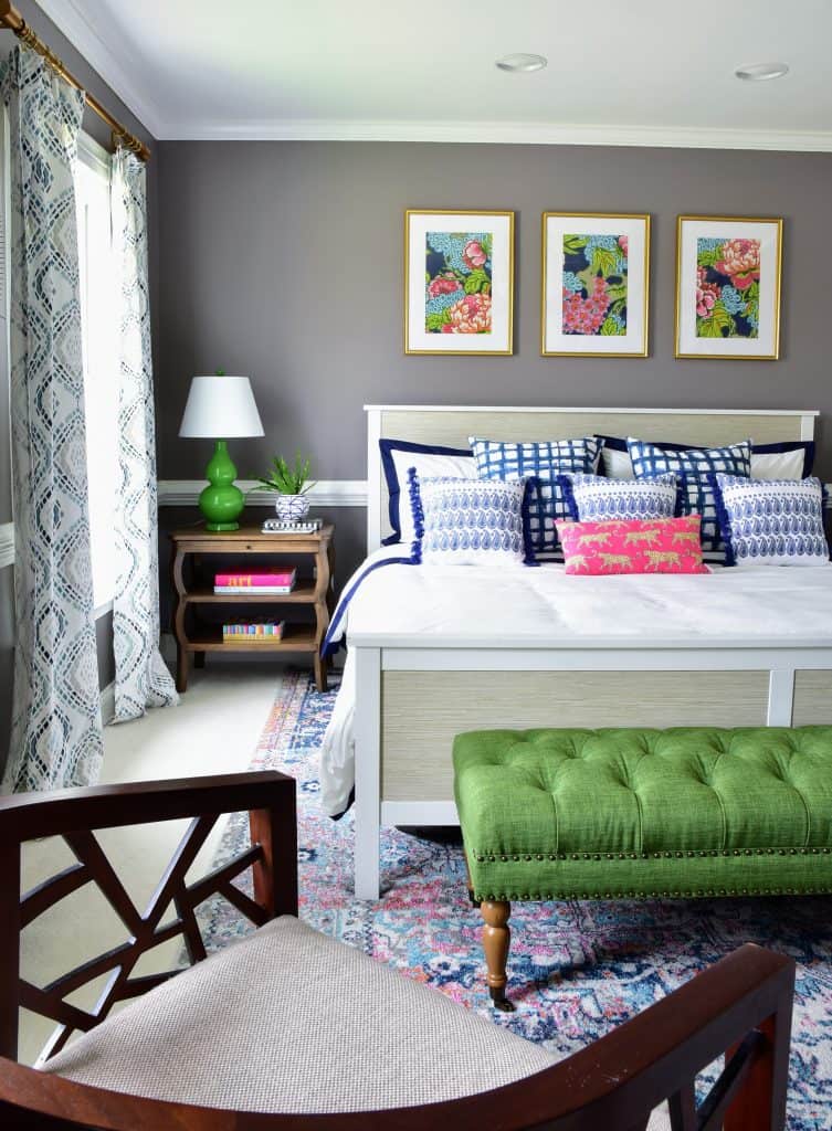 Another angle of our master bedroom makeover showing our queen bed, over the bed art, and colorful throw pillows, along with the small seating area at the foot of the bed.