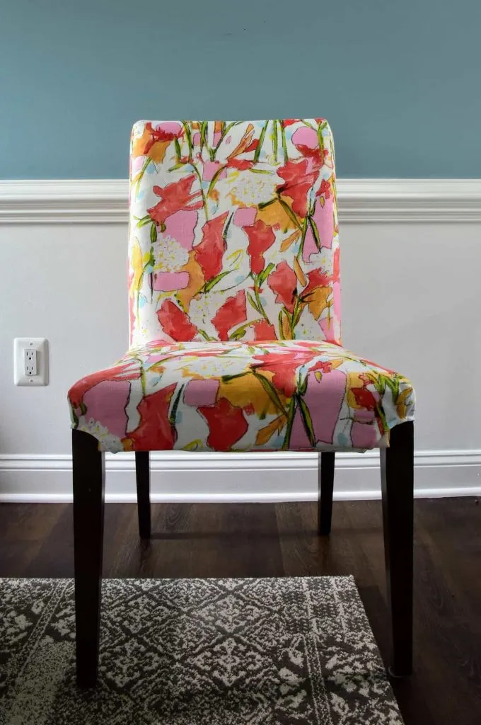 A dining room chair covered in a colorful abstract patterned seat cover from IKEA.