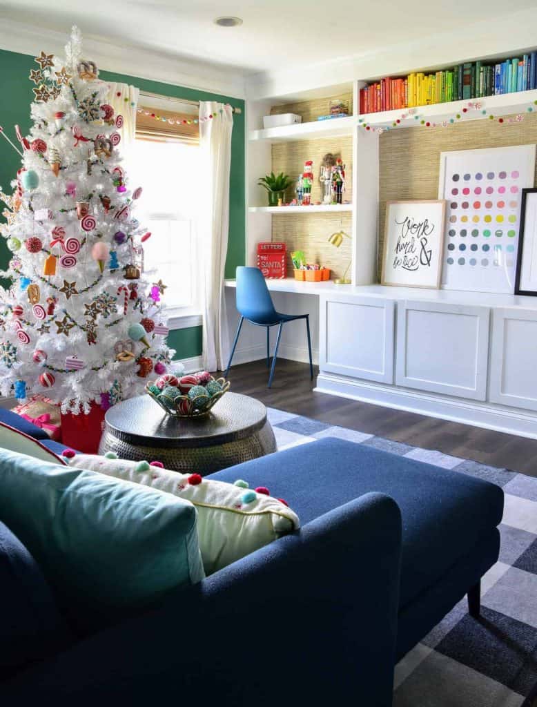 Our kids playroom, decorated for Christmas with a candy-themed Christmas tree filled with candy ornaments and decorations, garland hanging over the white built-in bookshelves, and colorful decor.