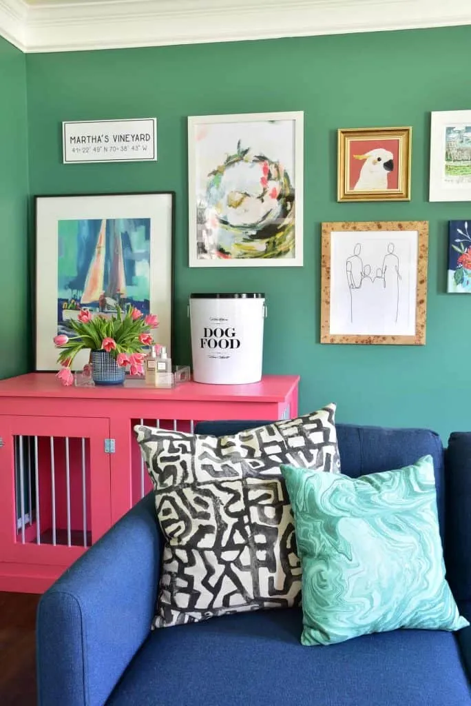 The art print wall in our updated kids playroom is painted a gorgeous hunter green and decorated with colorful framed art prints and a coral colored storage cabinet.