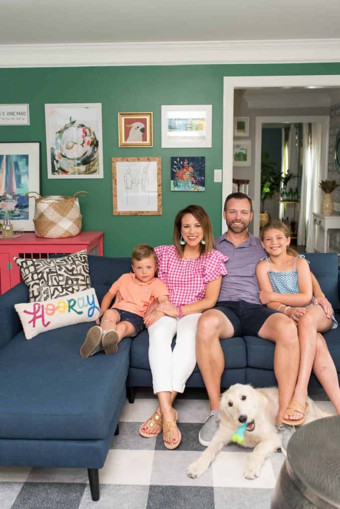 Mom, dad, and two kids kit on the navy blue couch in the updated kids playroom, smiling happily at the camera.